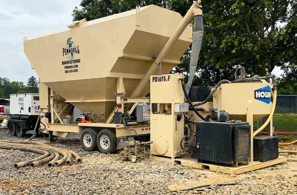 A large low-profile cement silo feeding a high shear colloidal grout plant on a jobsite with trees and a generator in the background.
