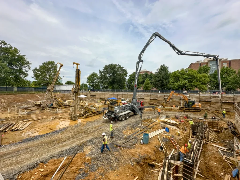 large job site with concrete pumping truck, 2 drill rigs, construction workers, and an excavator