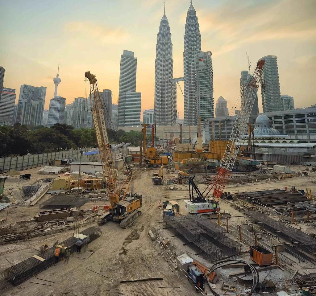 An aerial photo filled with heavy equipment on a jobsite with a background of large city skyscrapers and a sunset sky.