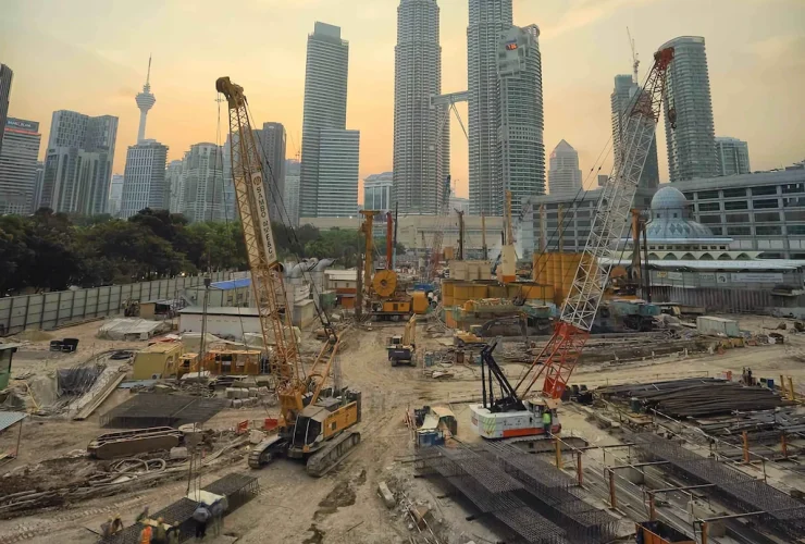 An aerial photo filled with heavy equipment on a jobsite with a background of large city skyscrapers and a sunset sky.