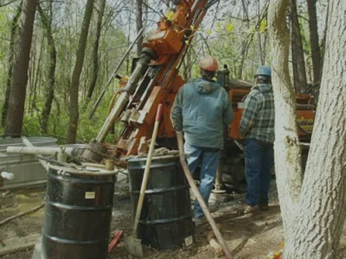 Three workers at a drilling rig site in the woods