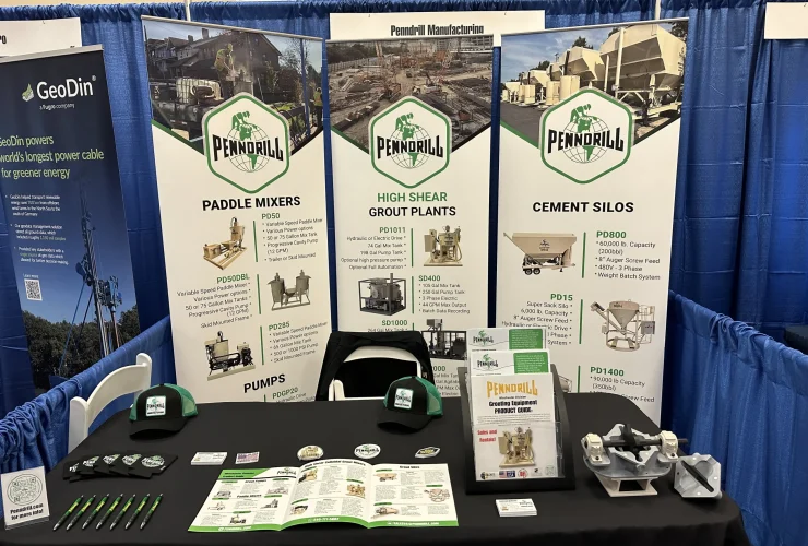 An exhibit booth with 3 white rollup banners and lots of stickers, brochures, and hats as giveaway items on the table.