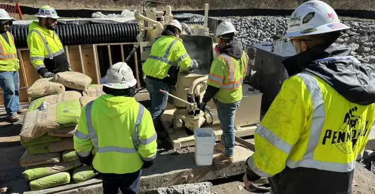 Man overlooking operator of grout mixer, providing training on grout mixer maintenance.