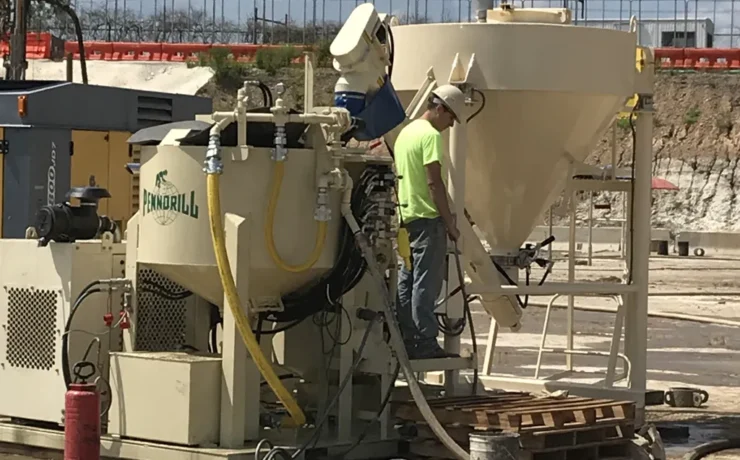 grout-mixer-maintenance-2 - Pennsylvania Drilling Company 2 pieces of heavy machinery grouting equipment including a grout mixer and grout silo with an operator standing on the operating deck.