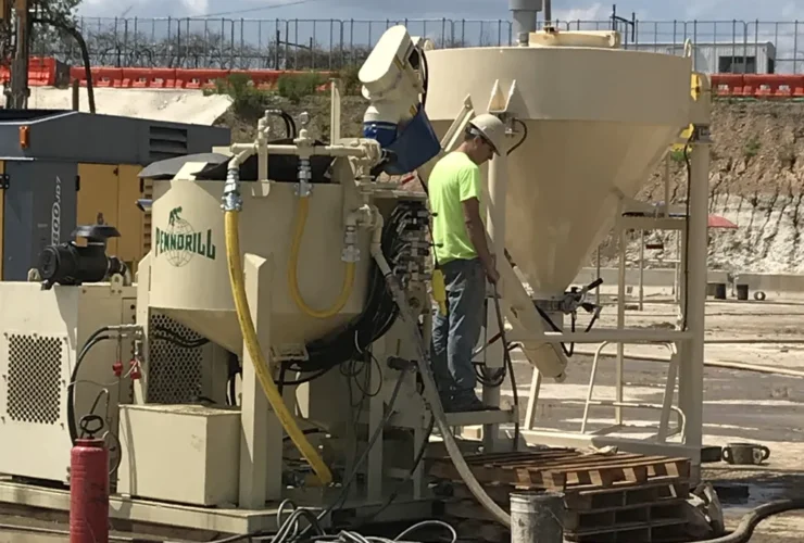 2 pieces of heavy machinery grouting equipment including a grout mixer and grout silo with an operator standing on the operating deck.