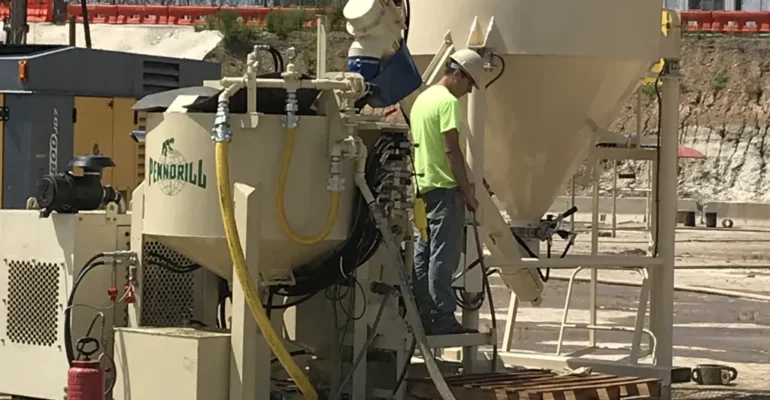 2 pieces of heavy machinery grouting equipment including a grout mixer and grout silo with an operator standing on the operating deck.