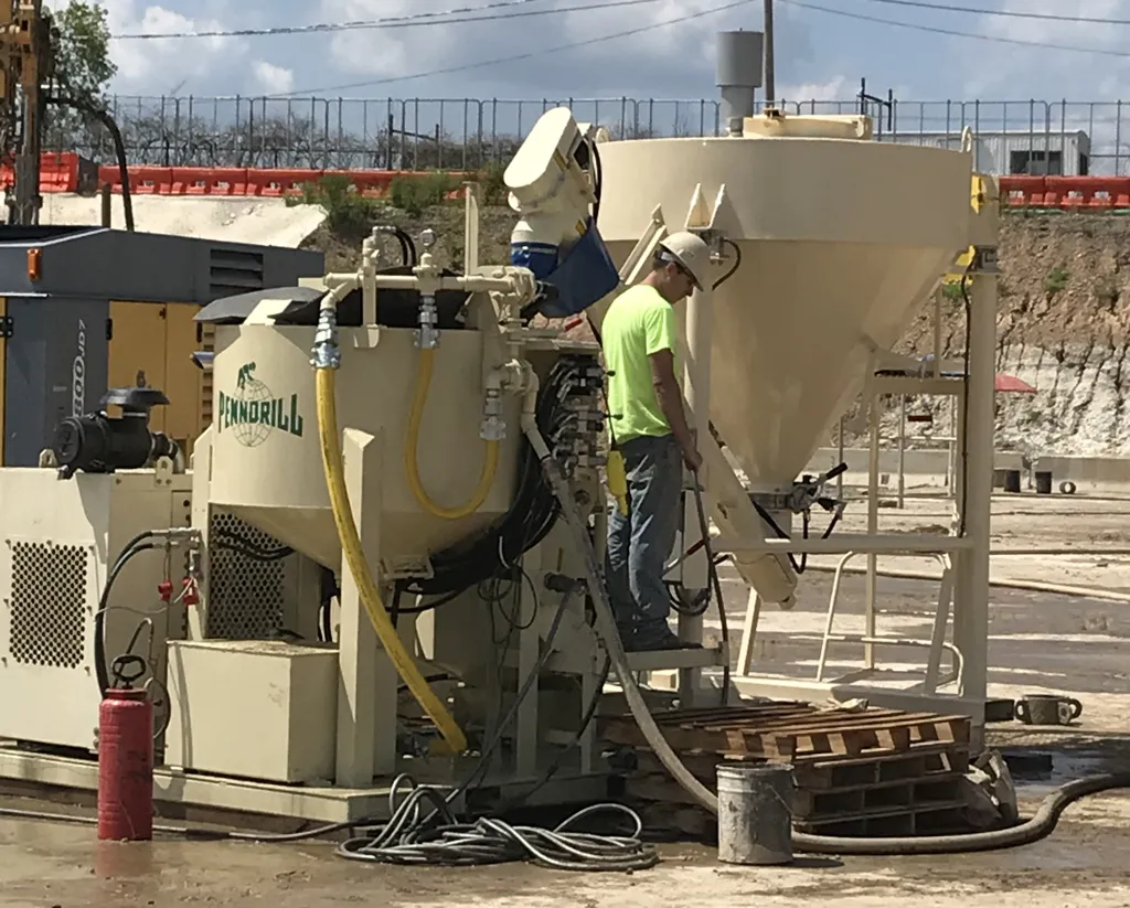 grout-mixer-maintenance-2 - Pennsylvania Drilling Company 2 pieces of heavy machinery grouting equipment including a grout mixer and grout silo with an operator standing on the operating deck.